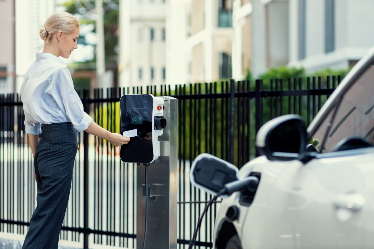 Frau lädt ihr Elektroauto an Ladestation auf.