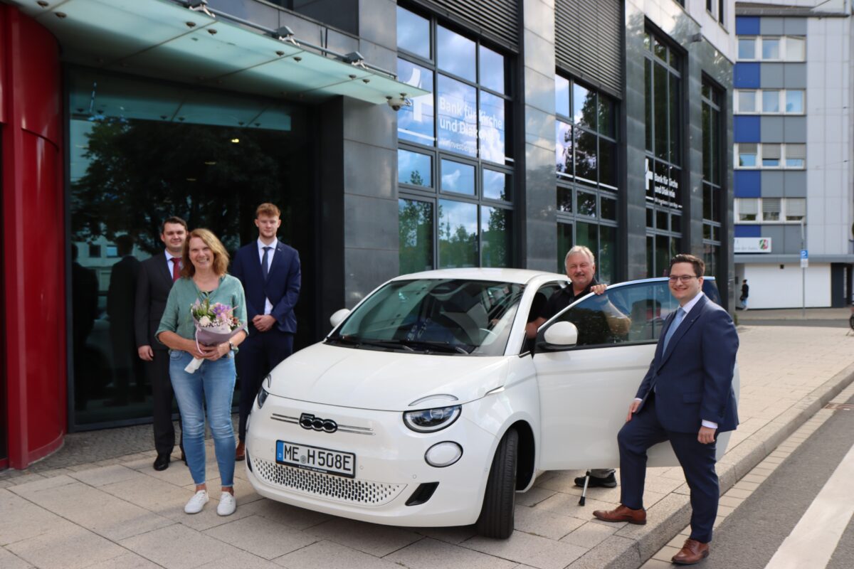 Ehepaar und Bankmitarbeitende stehen vor neuem Auto.