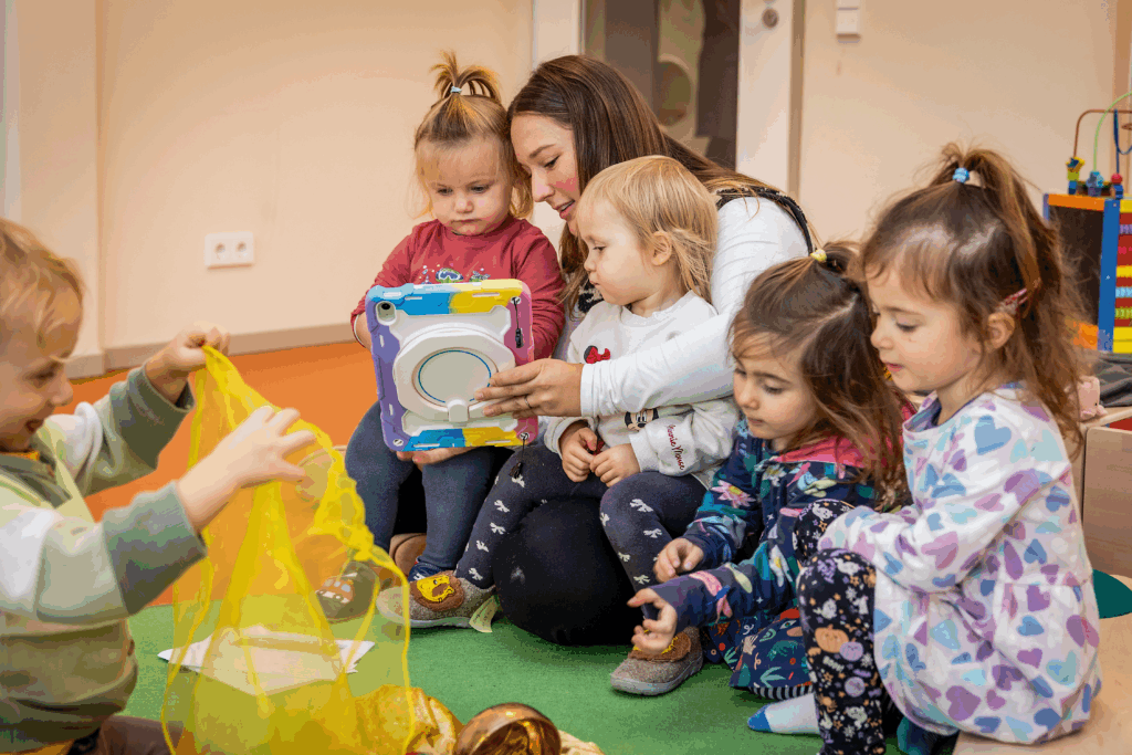 Frau schaut mit Kindergartenkindern auf Tablet.