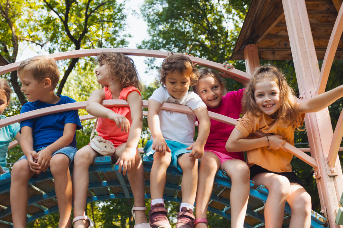 Kinder sitzen auf Holzbrücke auf dem Spielplatz.